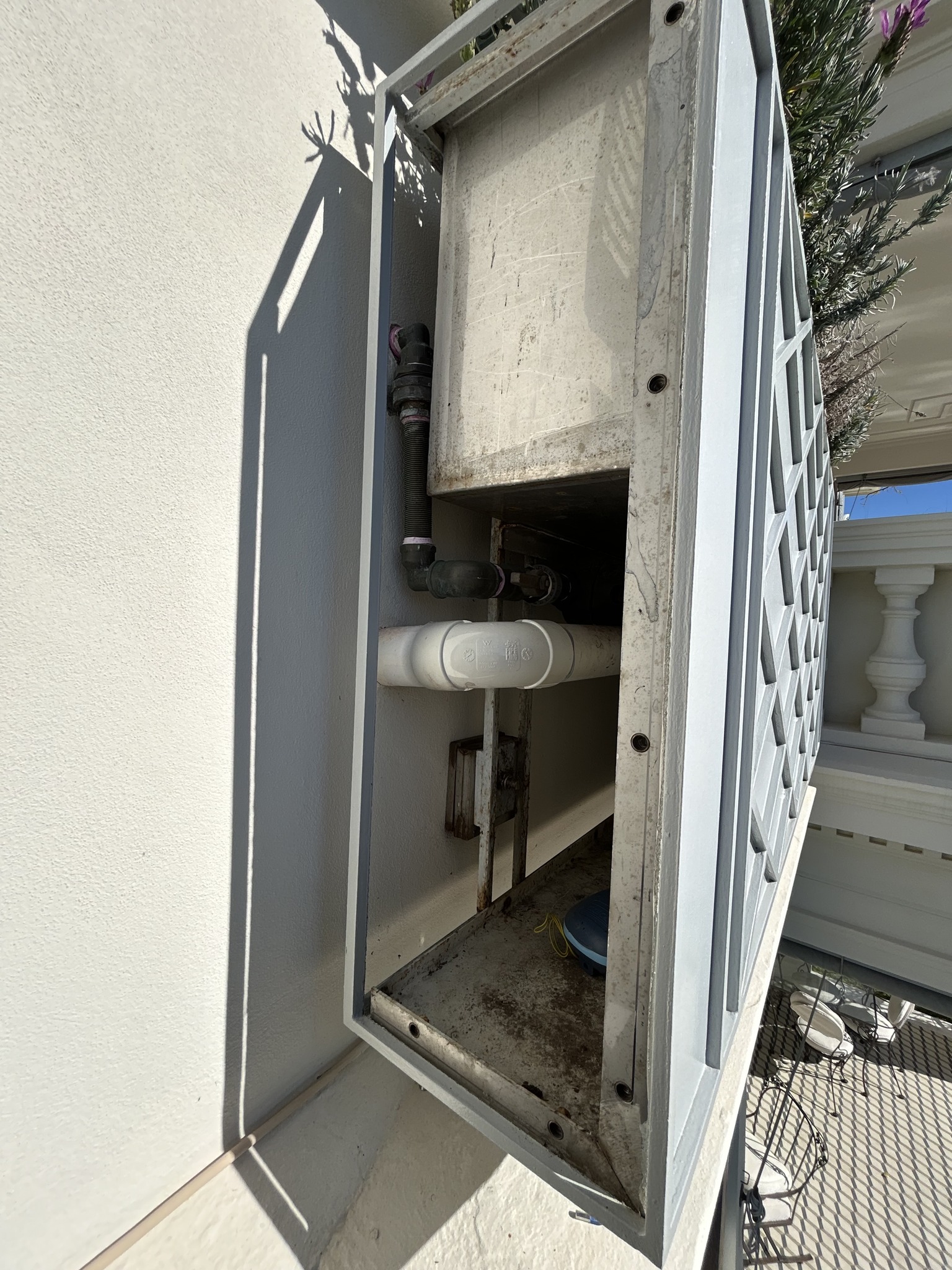 Steel planter enclosure with the access plate removed, exposing internal pipework.